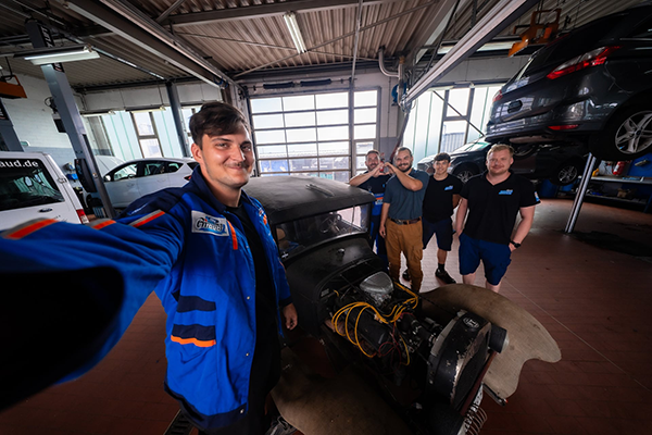 5 Motorenhelden vom Autocenter Giraud GmbH bei der Arbeit und lachen in die Kamera.