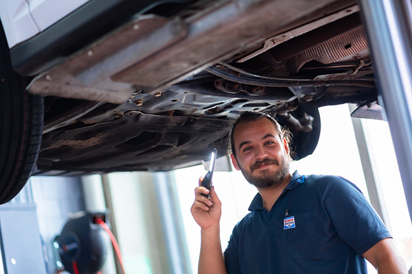 Ein Motorenheld vom Autocenter Giraud GmbH bei der Arbeit. Er lacht in die Kamera.